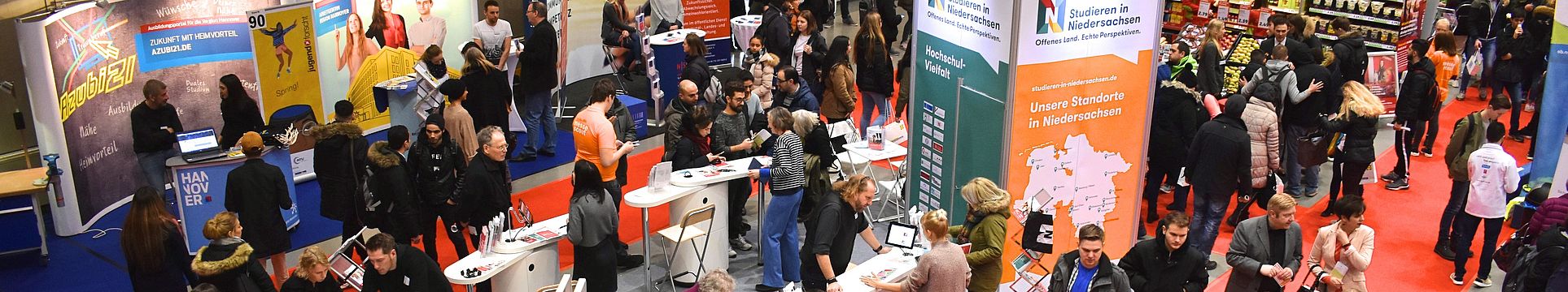 Eine Halle voll mit Ständen und Gästen bei der Messe Beruf und Bildung, im Mittelpunkt der Messestand von Studieren in Niedersachsen, an dem sich viele junge Menschen beraten lassen