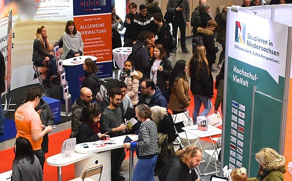 Eine Halle voll mit Ständen und Gästen bei der Messe Beruf und Bildung, im Mittelpunkt der Messestand von Studieren in Niedersachsen, an dem sich viele junge Menschen beraten lassen