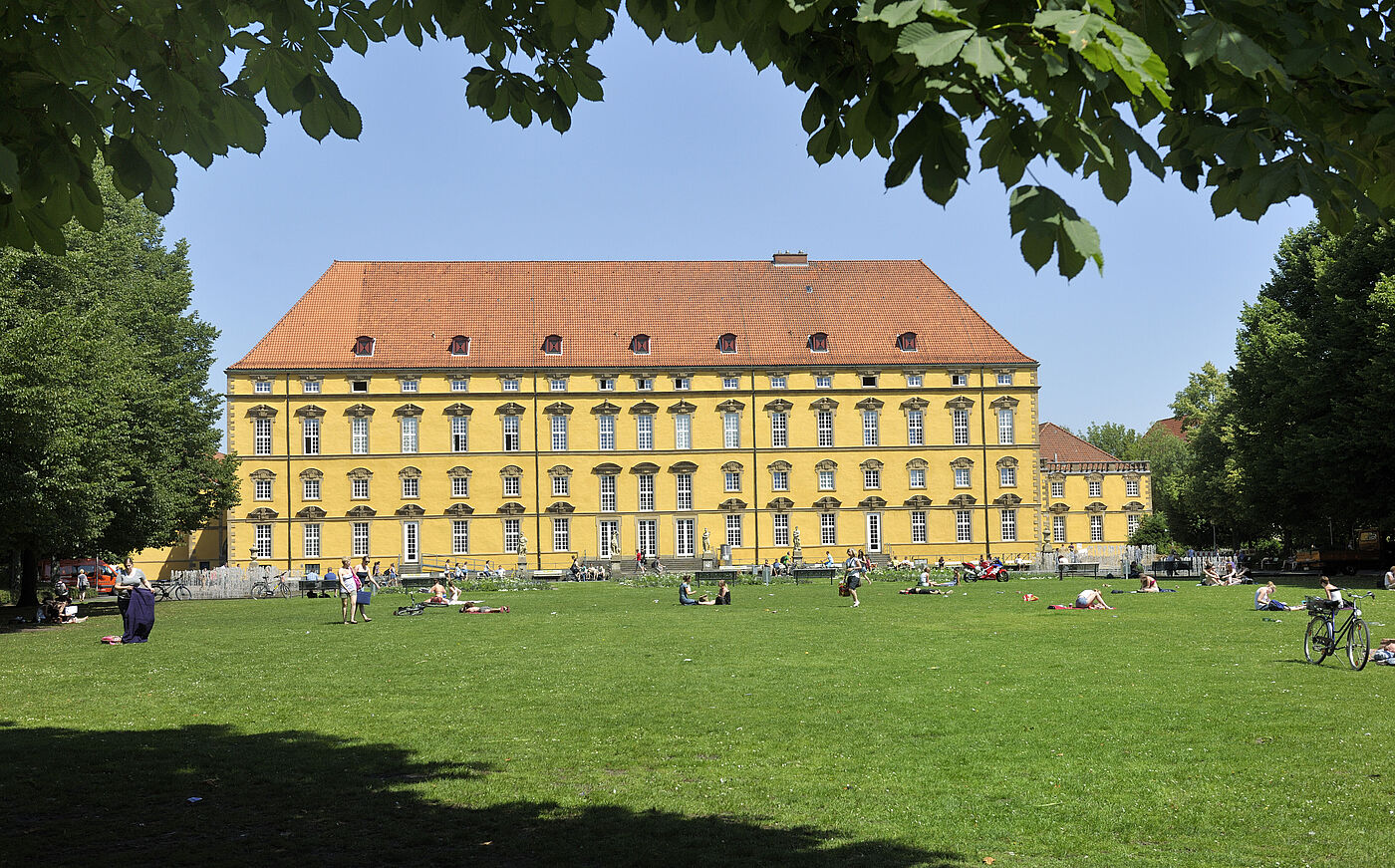 Studierende auf der Wiese vor dem historischen Hauptgebäude der Universität Osnabrück