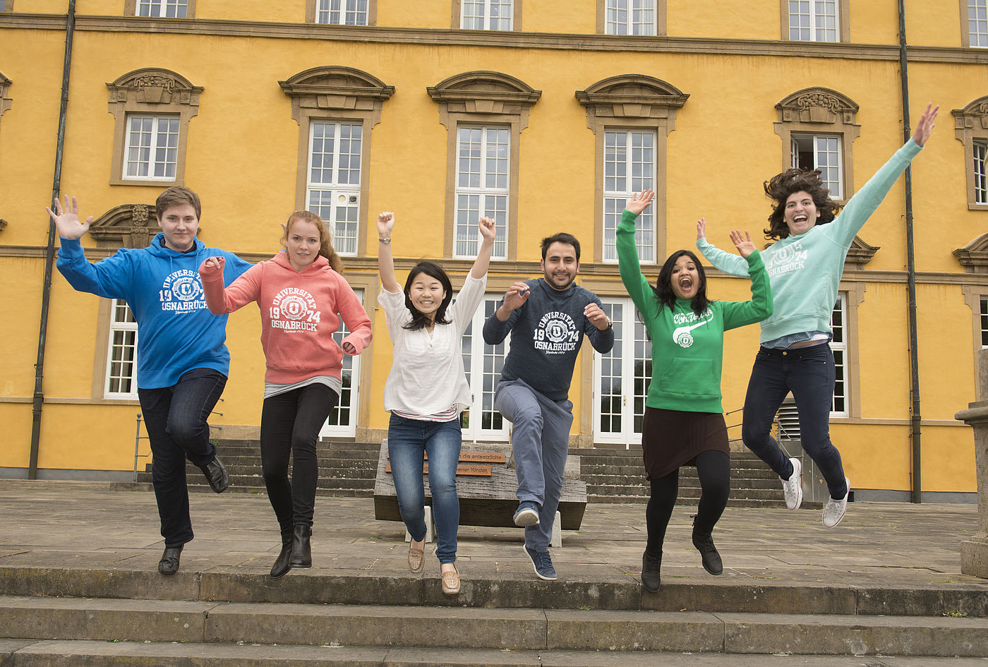 Studierende springen vor dem historischen Hauptgebäude der Universität Osnabrück jubelnd in die Luft