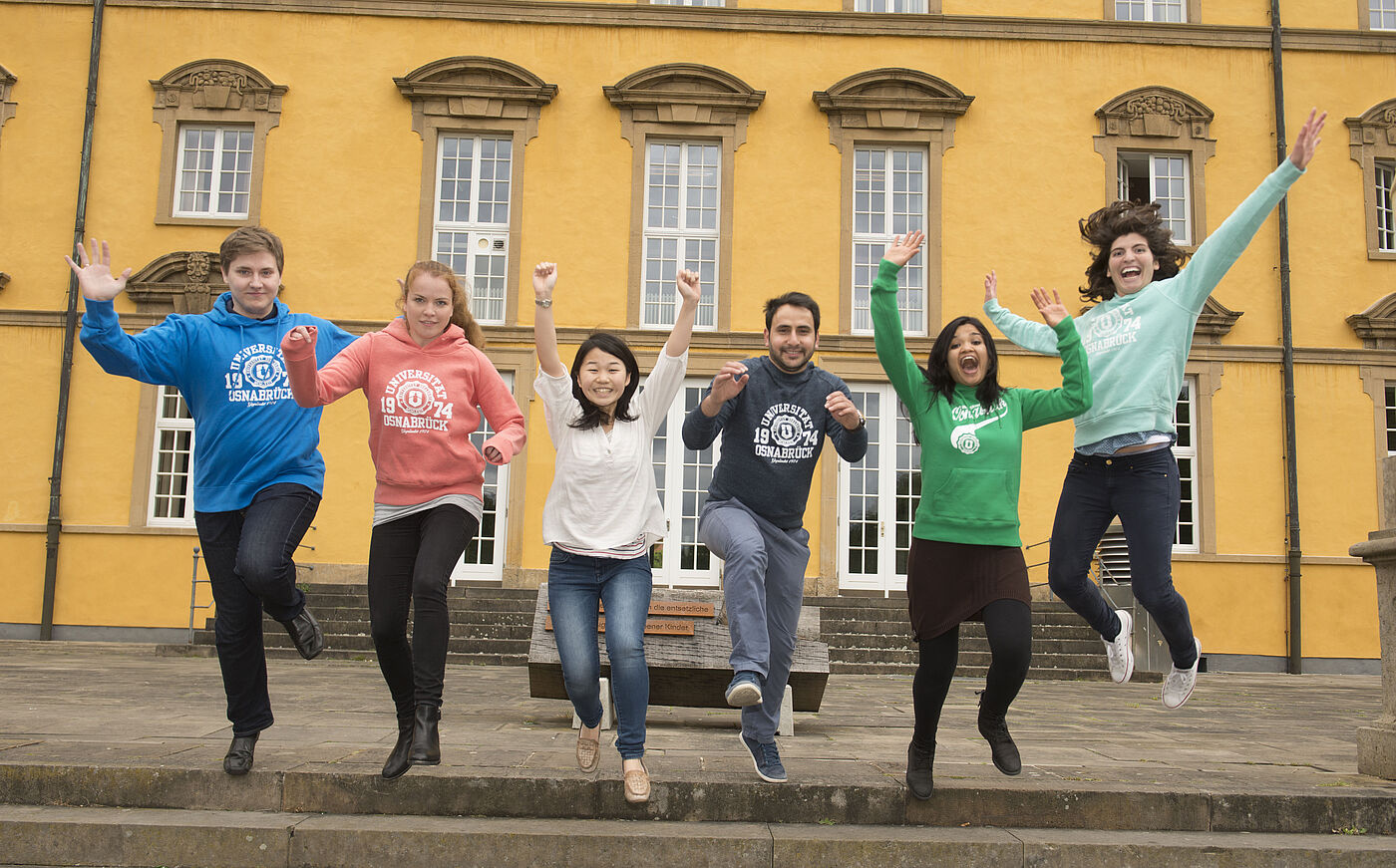 Studierende springen vor dem historischen Hauptgebäude der Universität Osnabrück jubelnd in die Luft