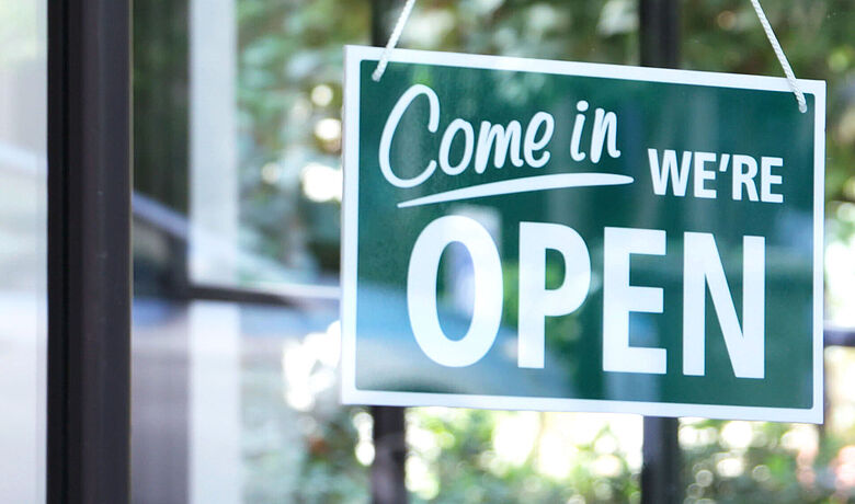 Ein grünes Schild hängt in einer Fensterfront, darauf steht: Come in, we're open