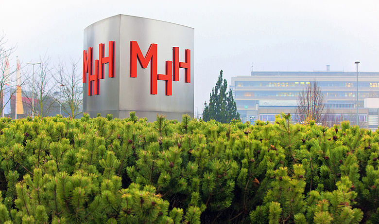 Stele mit dem Logo der MHH vor dem Hochschulgebäude