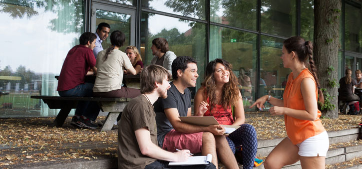 Studierende der Universität Lüneburg sitzen in Gruppen vor dem Hochschulgebäude zusammen