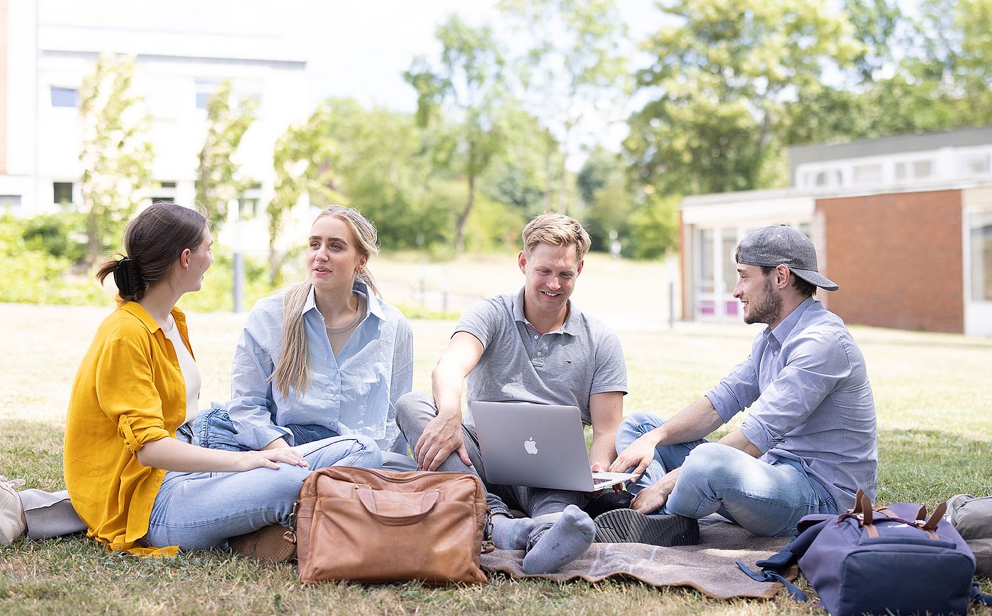 Studierende sitzen gemeinsam auf dem Rasen auf dem Campus Sammelsonplatz