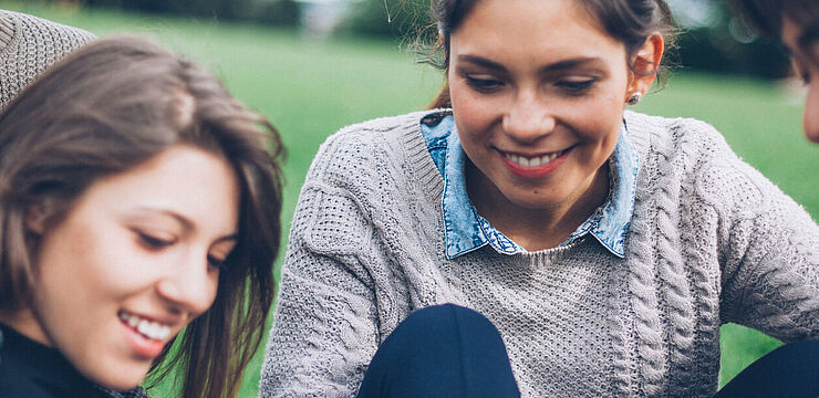 Auf einer Wiese sitzen mehrere junge Menschen zusammen und betrachten etwas auf einem Tablet-PC