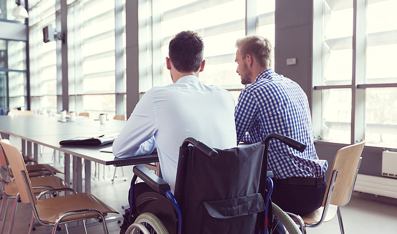 Zwei junge Menschen sitzen zusammen und lernen, einer sitzt in einem Rollstuhl 