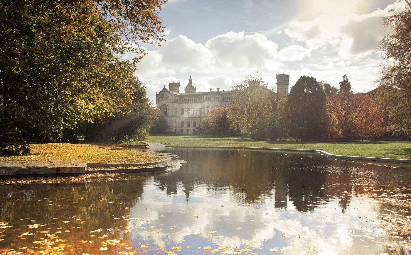 Das historische Hauptgebäude der Universität Hannover hinter einem herbstlichen Park mit See