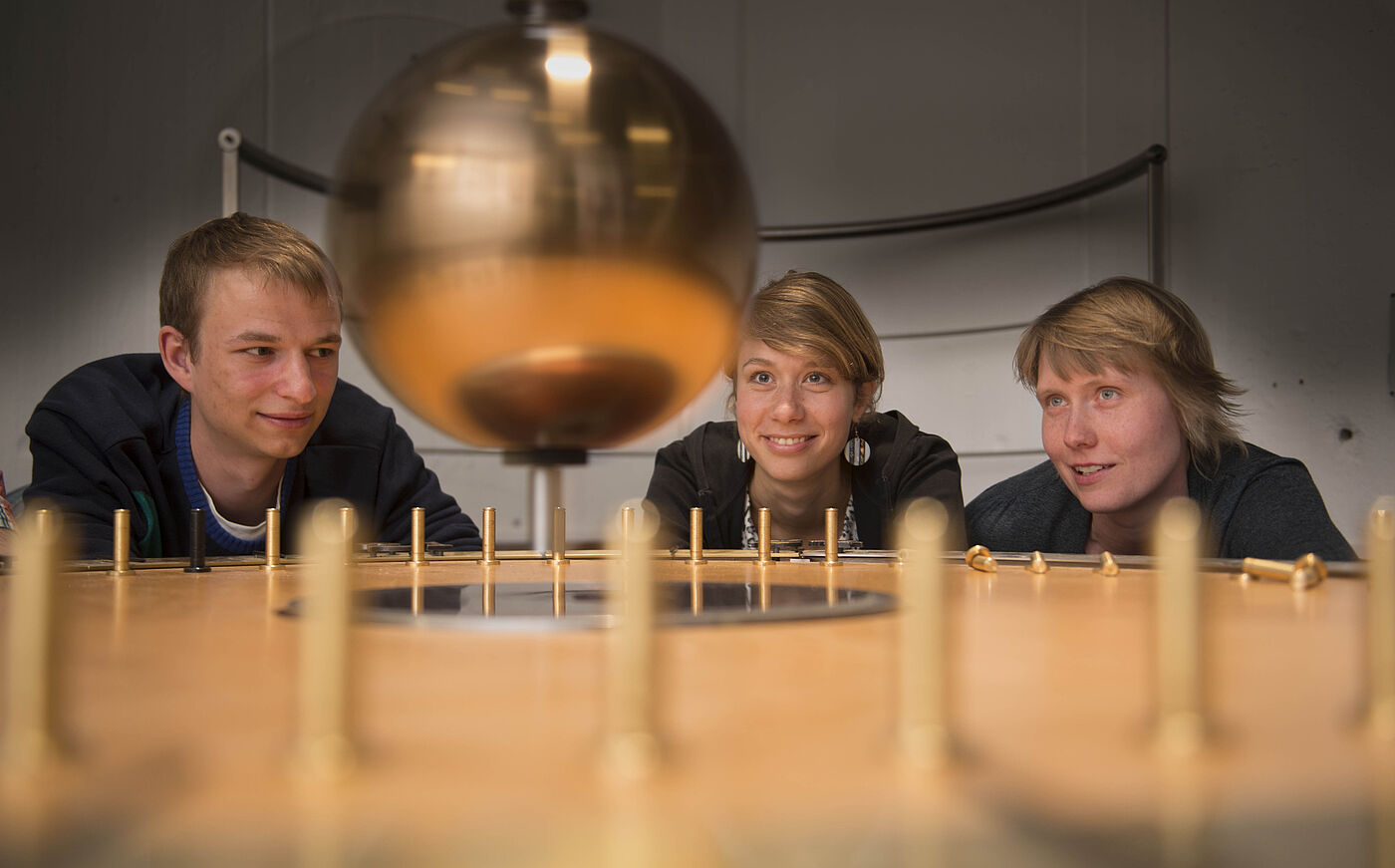 Drei Studierende beobachten das Foucault-Pendel an der Universität Osnabrück