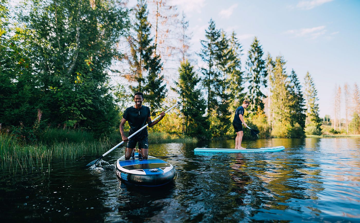 Zwei Studenten paddeln mit Stand Up Paddle Boards auf einem See