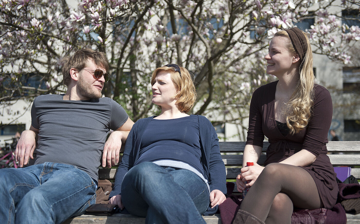 Studierende sitzen vorm Hochschulgebäude der HMTM Hannover unter Magnolienbäumen zusammen