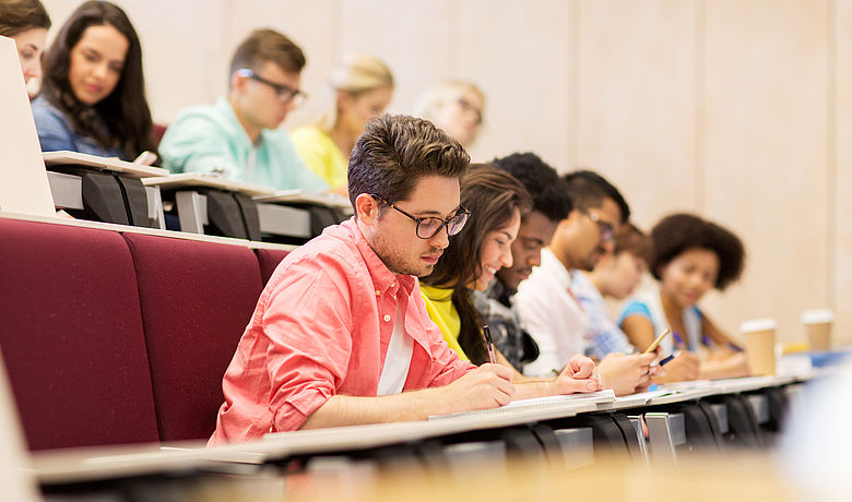 Viele junge Menschen mit unterschiedlichen Hautfarben sitzen schreibend in einem Hörsaal